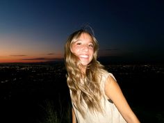 a woman standing on top of a lush green hillside next to a city at night