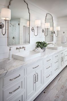 a white bathroom with double sinks and large mirrors on the wall, along with wooden floors