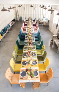 a long table is set up with colorful chairs and place settings for the dinner party