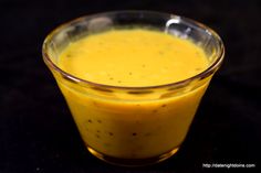 a glass filled with yellow liquid sitting on top of a black table next to a spoon