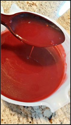 a spoon full of red liquid sitting on top of a white bowl