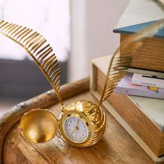 a golden clock sitting on top of a wooden table next to a stack of books