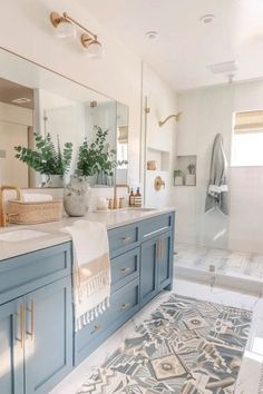 a large bathroom with blue cabinets and white counter tops, gold accents on the mirror