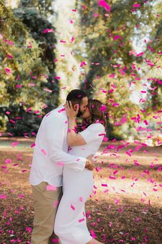 a man and woman kissing under pink confetti on the ground in front of trees