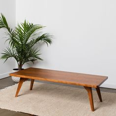 a wooden coffee table sitting on top of a rug next to a potted plant