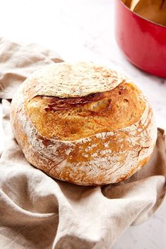 a loaf of bread sitting on top of a cloth next to a red pot filled with food