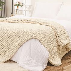 a large white blanket on top of a bed in a bedroom next to a plant