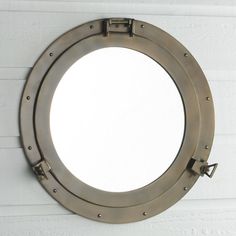 a metal porthole mirror mounted to the side of a white brick wall with an anchor hook