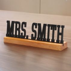 the word mrs smith spelled with black metal letters on a wooden stand in front of a white wall