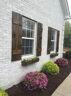 some flowers are in front of a white brick building with shutters on the windows