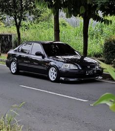 a black car is parked on the side of the road near some trees and bushes