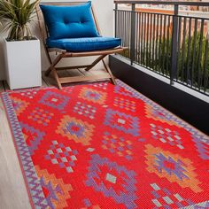 a bright red rug on a balcony next to a blue chair and potted plant