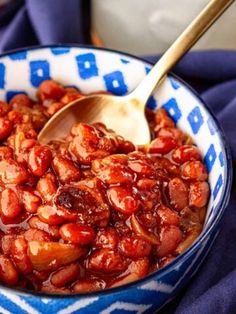 a blue and white bowl filled with beans on top of a purple table cloth next to a wooden spoon