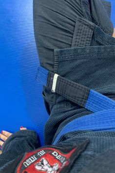 the back view of a person wearing a blue belt and black pants, with their feet on a blue mat