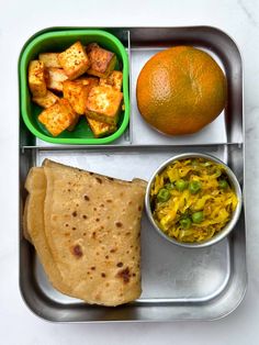 a metal tray topped with food and a bowl filled with oranges next to it