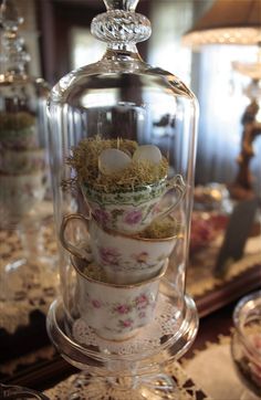 a glass clochet filled with cups and saucers on top of a table