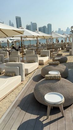 many lounge chairs and umbrellas on the beach with cityscape in the background