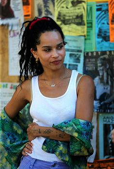 a woman with tattoos on her arm standing in front of a wall full of posters