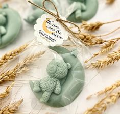 a small green teddy bear sitting on top of a piece of wax in front of some wheat