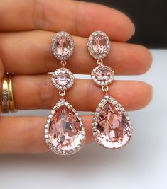 a pair of pink and white diamond earrings on someone's hand with gold rings