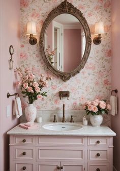 a bathroom with pink walls and flowers on the counter top, along with a large round mirror