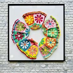 an art piece is displayed on a brick wall in front of a white frame with multicolored flowers