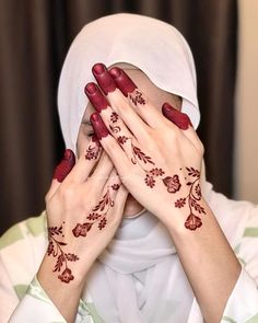 two hands covering their faces with red henna designs on each hand and the other