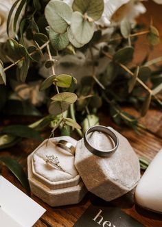 two wedding rings sitting on top of a box next to flowers and an open book