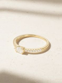 a gold ring with a heart shaped diamond on the front and side, sitting on a white surface