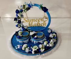 a blue and white cake with flowers on it, surrounded by two wedding rings that say sweet mahek