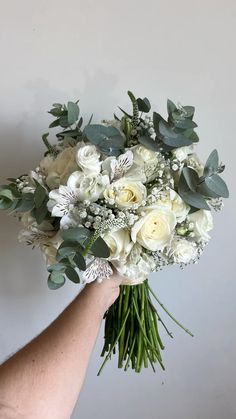 a bouquet of white flowers and greenery in someone's hand