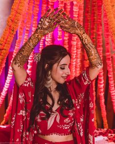 a woman in a red outfit holding her hands up above her head with flowers on the wall behind her