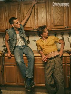 two men sitting on top of a kitchen counter next to each other with their arms in the air