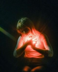 a woman sitting in the dark holding her hands together