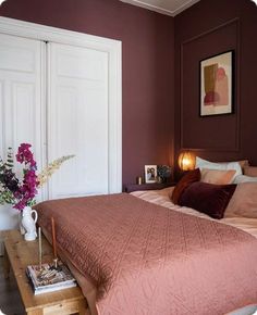 a bedroom with a bed, nightstands and pictures on the wall above it in purple tones