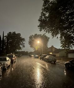 cars are parked on the side of the road in the rain at night with street lights shining