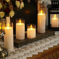 five lit candles on a tray in front of a vase with roses and other flowers