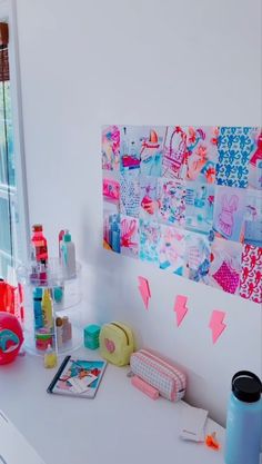 a white desk topped with lots of crafting supplies next to a window covered in pink and blue paper