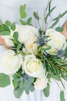 a bridal bouquet with white roses and greenery in the bride's hand