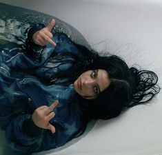 a woman laying down in a bathtub with her hand up to the side and pointing at something