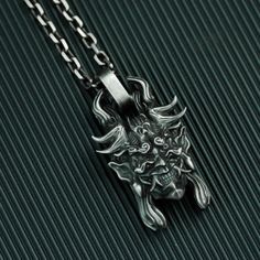 a silver necklace with an image of a demon on it