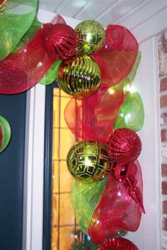 a christmas wreath with red, green and gold ornaments hanging from it's front door