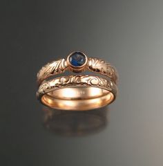 two gold wedding bands with blue stone in the center and leaves on each band, set against a black background