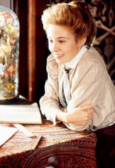 a woman sitting at a table with a book and glass jar on top of it