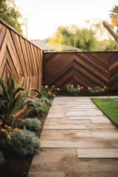 a wooden fence with grass and flowers in the foreground, next to a small garden