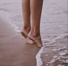 a woman walking along the beach with her feet in the water