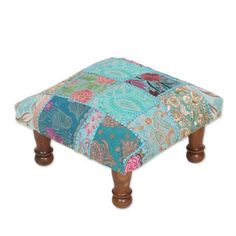 a patchwork foot stool with wooden legs and an upholstered seat cushion on it