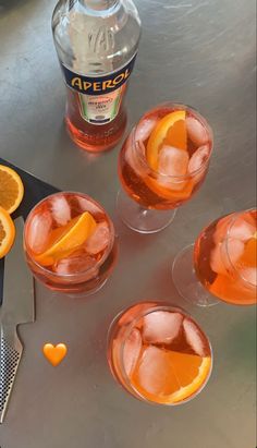 four glasses filled with oranges next to a bottle of aperoli wine and an orange slice