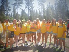 a group of young women standing next to each other in front of some pine trees