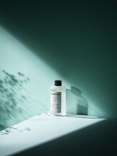 a bottle of lotion sitting on top of a table next to a shadow wall